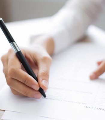 Cropped view of woman holding pen and filling out application form at table with focus on hand with pen